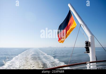 Borkum, Deutschland. Juni 2024. Eine Flagge der Bundesrepublik Deutschland fliegt auf einer Fähre der AG Ems während der Überfahrt zur Insel Borkum. Die Reederei betreibt den Fährdienst von Emden und dem niederländischen Hafen Eemshaven zur westlichsten Nordseeinsel Deutschlands. Quelle: Hauke-Christian Dittrich/dpa/Alamy Live News Stockfoto