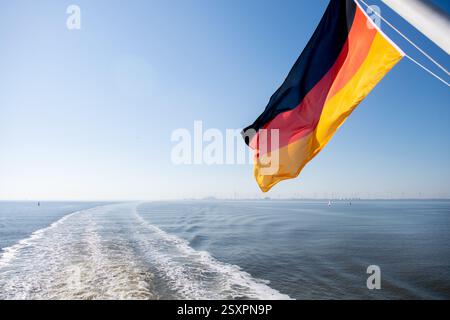 Borkum, Deutschland. Juni 2024. Eine Flagge der Bundesrepublik Deutschland fliegt auf einer Fähre der AG Ems während der Überfahrt zur Insel Borkum. Die Reederei betreibt den Fährdienst von Emden und dem niederländischen Hafen Eemshaven zur westlichsten Nordseeinsel Deutschlands. Quelle: Hauke-Christian Dittrich/dpa/Alamy Live News Stockfoto