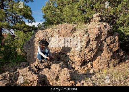 Frau, die blaue Jeans und Cowboyhut auf großen Steinen hockt, Lumberton, Rio Arriba County, New Mexico, USA. Stockfoto