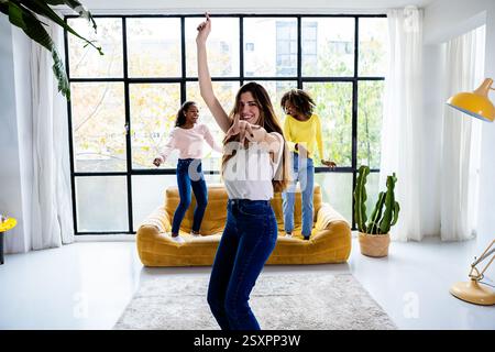 Junge Frauen tanzen im Wohnzimmer: Freundschaft und freudige Momente feiern Stockfoto