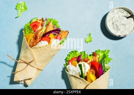Griechische Huhn-Gyro-Wraps mit Salat, Tomaten, Gurken und Tzatziki-Sauce auf blauem Hintergrund, Draufsicht. Gesundes griechisches Essen. Döner-Hühnchen-Döner-Kebab Stockfoto