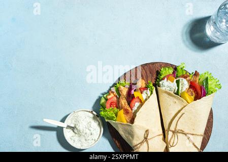Griechisches Hühnchen-Souvlaki-Wraps mit Gemüse und Tzatziki-Sauce auf blauem Hintergrund, Draufsicht, Kopierraum. Griechisches Gyros Essen. Döner-Döner in Pita-Brot. Stockfoto