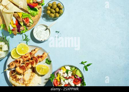 Griechische Essensauswahl. Huhn Gyros Wrap, Souvlaki, Pita, griechischer Salat, Tzatziki, Fetakäse, Oliven für gesundes Mittagessen auf blauem Hintergrund, Kopierraum Stockfoto