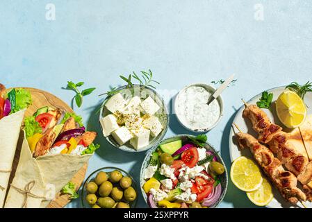 Griechische Essensauswahl. Huhn Gyros Wrap, Souvlaki, Pita, griechischer Salat, Tzatziki, Fetakäse, Oliven für gesundes Mittagessen auf blauem Hintergrund, Kopierraum Stockfoto