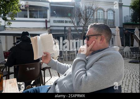 Portugal, Algarve; Fuseta. Mann liest in einem Café auf dem Stadtplatz Stockfoto