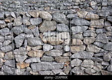 Abstrakter Hintergrund einer Gabionenwand aus Granitsteinen und Drahtgeflecht Stockfoto