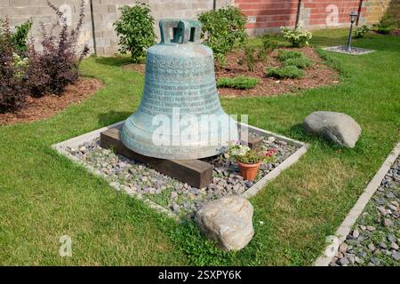 Alte große, antike Bronzeglocke mit Inschriften, ausgestellt auf dem Boden in der Nähe der Kirche St. Michael Erzengel in Ivenets, Weißrussland, umgeben von b Stockfoto