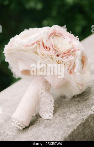 Ein zarter Blumenstrauß aus Stoffblumen mit rosa und weißen Tönen liegt wunderschön auf einer Steinoberfläche im Freien. Stockfoto