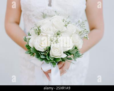Wunderschöner weißer Rosenstrauß, gehalten von einer Braut in einem Brautkleid mit Spitze vor neutralem Hintergrund Stockfoto