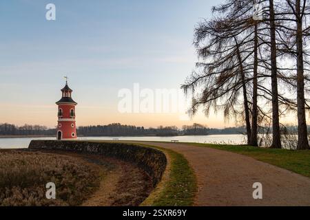 Leuchtturm am See bei Moritzburg bei Sonnenuntergang, mit warmem, glühendem Himmel, der sich auf dem Wasser spiegelt. Die Silhouette des Schlosses im Hintergrund fügt Charme und Ruhe hinzu Stockfoto