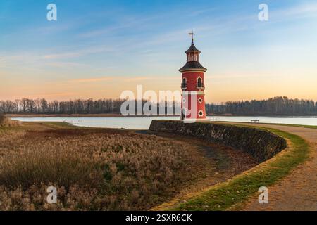 Leuchtturm am See bei Moritzburg bei Sonnenuntergang, mit warmem, glühendem Himmel, der sich auf dem Wasser spiegelt. Die Silhouette des Schlosses im Hintergrund fügt Charme und Ruhe hinzu Stockfoto