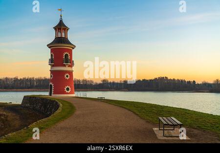 Leuchtturm am See bei Moritzburg bei Sonnenuntergang, mit warmem, glühendem Himmel, der sich auf dem Wasser spiegelt. Die Silhouette des Schlosses im Hintergrund fügt Charme und Ruhe hinzu Stockfoto