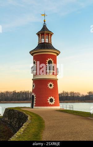 Leuchtturm am See bei Moritzburg bei Sonnenuntergang, mit warmem, glühendem Himmel, der sich auf dem Wasser spiegelt. Die Silhouette des Schlosses im Hintergrund fügt Charme und Ruhe hinzu Stockfoto