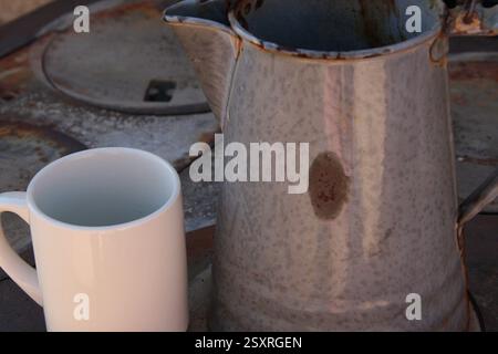 Eine alte Kaffeekanne aus Metall und eine Keramikschale stehen auf einem altmodischen Herd. Stockfoto