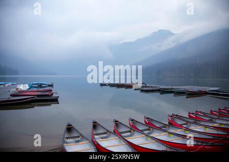 Rote Kanus stehen am Ufer eines nebelverhangenen Sees, bereit für Abenteurer, um das ruhige Wasser zu erkunden Stockfoto