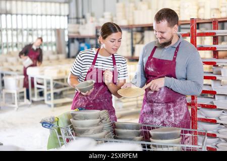 Kollegen in der Keramikwerkstatt diskutieren über eine Reihe von Slipcast-Töpferwaren Stockfoto