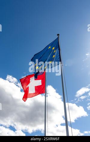 Die Fahnen der Schweiz und der EU wehen im Wind unter dem sonnigen blauen Himmel Stockfoto