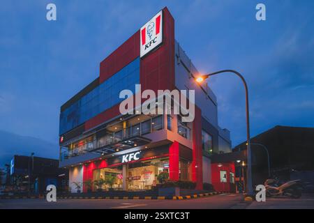 Balikpapan, Indonesien - 22. Februar 2025. Ein mehrstöckiges KFC-Gebäude in der Abenddämmerung mit einer rot-grauen Fassade mit dem KFC-Logo, großen Fenstern und einer Beleuchtung Stockfoto