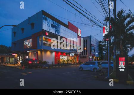 Balikpapan, Indonesien - 22. Februar 2025. Äußere des KFC Balikpapan Gebäudes in der Abenddämmerung, eine rot-graue Fassade, ein Schild mit dem KFC-Logo und dem Wort M Stockfoto