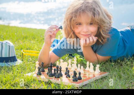 Der Junge zeigt Schachfiguren auf einem Schachbrett. Kluges, konzentriertes und denkendes Kind, das Schach spielt. Stockfoto