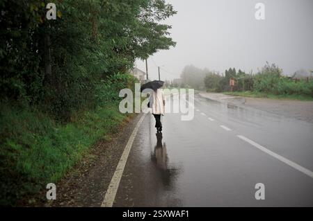 Nebelige Landstraße mit Frau, die im Regen läuft, Bistrica, Bosnien-Herzegowina Stockfoto