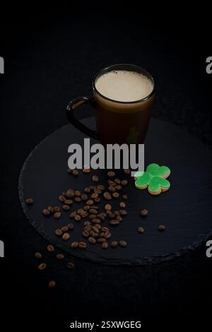 Eine Tasse irischer Kaffee, kleeförmiger Keks und Kaffeebohnen auf schwarzem Hintergrund Stockfoto