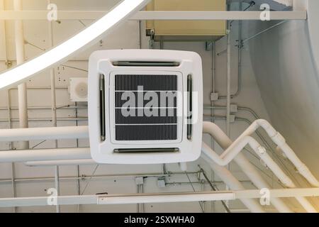 Eine Deckenklimaanlage ist in einem hellen industriellen Ambiente untergebracht. Rohre und Belüftungssysteme sind um das Gerät herum sichtbar, Emphas Stockfoto