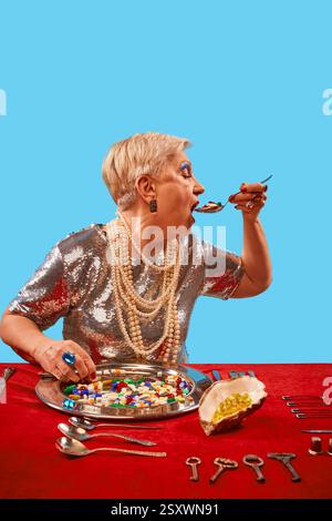 Ältere Frau in glamourösem silbernem Kleid, die Pillen aus silbernem Tablett auf leuchtendem blauem Hintergrund isst. Alternder Lebensstil. Pop-Art-Fotografie Stockfoto