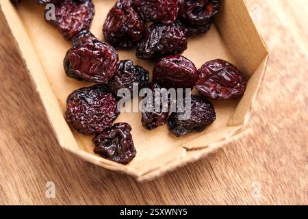 Getrocknete Kirschen in kleiner Pappschachtel auf Holzoberfläche. Faltige, dehydrierte nahrhafte Beeren. Bio gesunder Snack. Draufsicht. Stockfoto