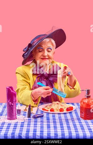 Ältere Frau in gelbem Blazer mit blauem Hut, der Spaghetti mit Plastikkamm hält, während sie vor rosa Hintergrund lächelt. Stockfoto