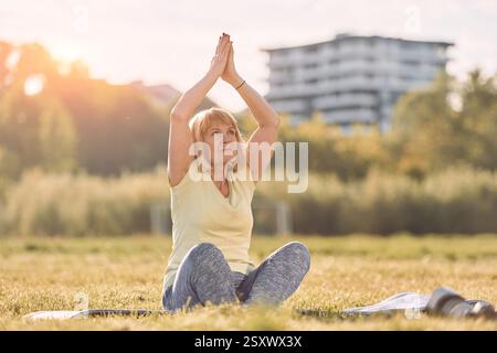 Auf Yogamatte. Seniorin hat ein schönes Wochenende draußen auf dem Feld an sonnigen Tagen. Stockfoto