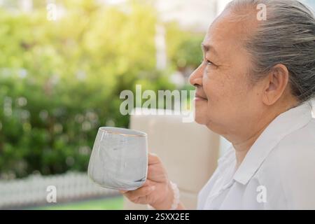 Seitenporträt einer älteren asiatischen Frau, die zu Hause im Garten eine Tasse Kaffee hält. Kopierbereich. Stockfoto