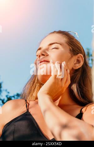 Frau, Sonne, Porträt: Nahaufnahme einer Frau mit geschlossenen Augen, die die Sonne im Freien genießt. Stockfoto