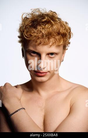 Selbstbewusster junger Mann mit lockigem Haar und Schmuck posiert stilvoll und spiegelt moderne Modetrends wider. Stockfoto