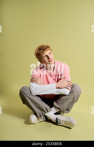 Ein junger Mann sitzt mit überkreuzten Beinen, durchdacht und stilvoll vor einem hellen Hintergrund. Stockfoto
