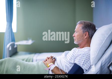 Älterer Mann ruht im Krankenhausbett, schauend nachdenklich und entspannt, Kopierraum Stockfoto