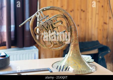 Ein französisches Horn aus Messing mit abgenutzter Patina liegt auf einem Holztisch in gemütlicher Atmosphäre. Stockfoto