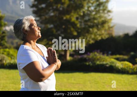 Seniorin meditiert draußen im friedlichen Garten, genießt Morgensonne, Kopierraum Stockfoto