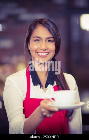 Lächelnder Barista auf roter Schürze serviert Kaffee in einem gemütlichen Café Stockfoto