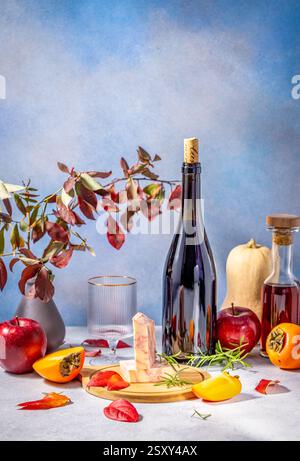 Gemütliches Stillleben im Herbst mit einer Flasche Rotwein, Käse, Äpfeln, Persimmons und einem Kürbis, er erinnert an die Wärme und Fülle der Herbsternte Stockfoto