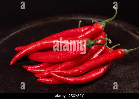 Leuchtend rote Chilischoten glitzern mit Wassertröpfchen, die auf einer dunklen Oberfläche aufgehäuft sind und ein beeindruckendes Bild von Frische und Würze schaffen Stockfoto