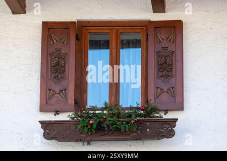 Traditionelles Alpenfenster mit dekorativen Holzläden und Winterdekoration. Europäischer rustikaler Stil und Gemütlichkeit Stockfoto