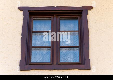 Antikes Holzfenster mit geschnitztem Rahmen - klassisches Fenster mit durchbrochenen Vorhängen vor einer warmen strukturierten Wand Stockfoto