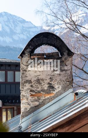 Klassischer Ziegelschornstein gegen Berge - klassischer Schornstein mit verbrannten Kanten und Rissen gegen schneebedeckte Gipfel Stockfoto