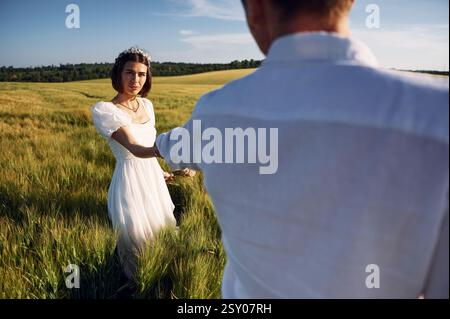 Halten sich gegenseitig an den Händen. Das Paar hat gerade geheiratet. Zusammen auf dem majestätischen Ackerfeld am sonnigen Tag. Stockfoto
