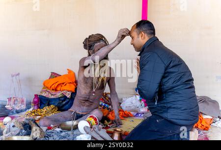 Ein geweihter, der göttliche Gnade von Naga Sadhu bei Mahakumbh-Treffen sucht Stockfoto