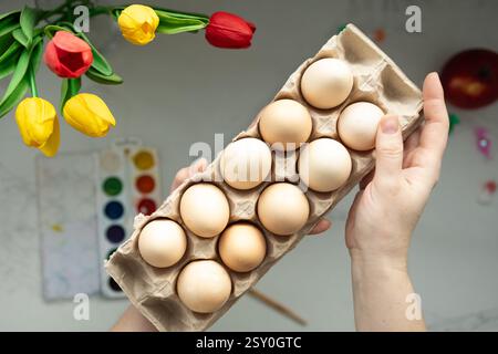 Eine wunderschöne Ausstellung frischer, biologischer Eier wird über lebendigen Tulpen und farbenfrohen Aquarellfarben gehalten Stockfoto