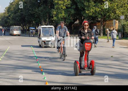 Segway im öffentlichen Park der Villa Borghese, Rom, Italien. Rom, Italien - 3. März 2019: Im öffentlichen Park der Villa Borghese reist eine Frau mit Segway, einige Touristen auf Fahrrädern, eine Familie mit einem kleinen Elektroauto. Im Hintergrund in der von Bäumen gesäumten Allee ein elektrischer Zug mit Touristen und ein Rollstuhl mit Pedal. Ein ruhiger Sonntag an einem sonnigen Tag in der italienischen Hauptstadt. Rom, Rom RM Italien Copyright: XG. Leonardix Stockfoto