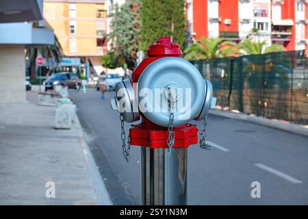 Hellroter Feuerhydrant steht auf einer sonnigen Stadtstraße, umgeben von Grün. Stockfoto
