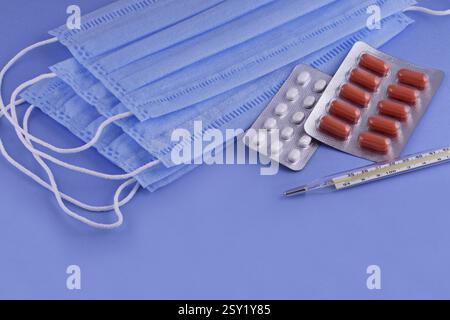 Medizinische Schutzmaske, Pillen, Thermometer auf blauem Hintergrund, Coronavirus-Schutz, Konzept einer Prävention und Behandlung Coronavirus, covid19 PR Stockfoto